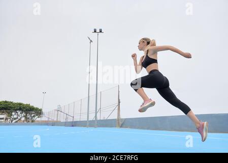 Vista lateral en ángulo bajo de una atleta joven segura en el equipo de fitness saltar en el terreno deportivo Foto de stock