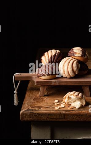 Pan de concha tradicional recién horneado colocado en tabla de madera sobre fondo negro