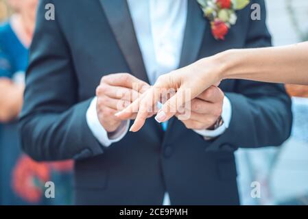 El novio en una chaqueta azul oscuro con un arreglo floral para la solapa del novio pone un anillo en la mano de la novia. Primer plano de recorte del pecho Foto de stock