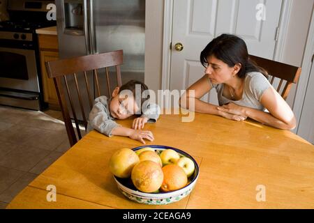 La madre hispana se sienta en la mesa de la cocina con su enojado hijo de cuatro años. SR. ©Bob Daemmrich