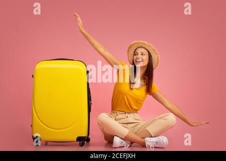Chica sentada al lado de la maleta, imitando el avión Foto de stock