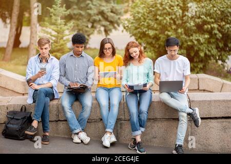 Estudiantes aprendiendo usando gadgets sentados al aire libre en el Campus Universitario Foto de stock