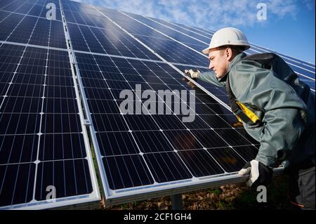 Trabajador profesional, con traje protector, casco y guantes, instalando baterías solares fotovoltaicas en un día soleado. Concepto de energía alternativa y recursos sostenibles de energía.