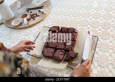 Mujer cortando brownies recién horneados en la rejilla de enfriamiento Foto de stock