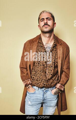 lengua arco hipocresía Modelo masculino de moda con tatuajes con un moderno abrigo sobre leopardo  camisa y jeans de pie contra fondo beige y mirando cámara con las manos en  el bolsillo Fotografía de stock -