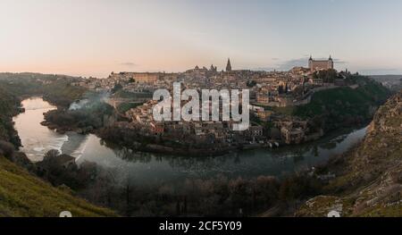 Vista panorámica sobre el río de la ciudad vieja de Toledo en España con castillos medievales y fortalezas al atardecer con nublado cielo y reflexión en el agua del río