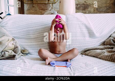 Niño jugando en turbante rosa sin ropa sentada en el sofá en la postura del  loto que cubre la cara Fotografía de stock - Alamy