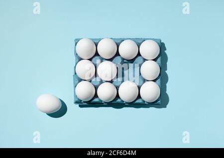 Vista superior de los huevos blancos colocados en la bandeja de papel demostrando concepto de diferencia sobre fondo azul en estudio Foto de stock