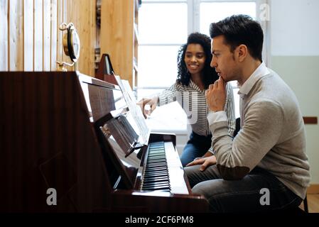 Joven aprendiendo a tocar el piano cerca de la mujer negra enseñando en estudio de música