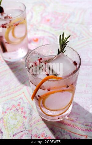 Cóctel tónico de Ginebra con agua tonificante rosa, pimienta rosa, romero, menta, canela, limón y naranja bajo la luz del sol en una mesa de restaurante Foto de stock