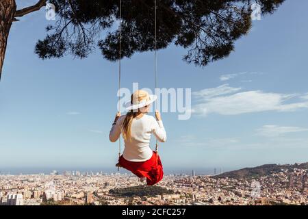chica divertirse con la falda roja y el sombrero balanceándose mientras contempla la ciudad en el fondo Foto de stock