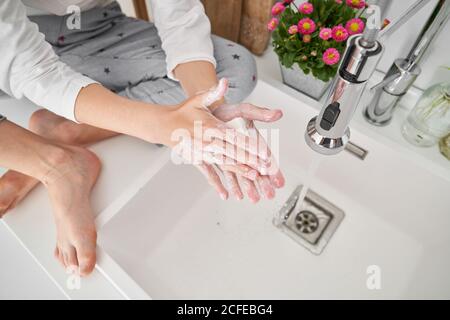 Niño rubio lavándose las manos en el fregadero de la cocina prevenir cualquier infección Foto de stock