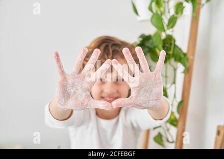 Niño rubio lavándose las manos en el fregadero de la cocina prevenir cualquier infección Foto de stock