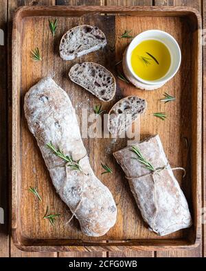 Vista superior de delicioso pan italiano ciabatta servido en madera bandeja con pote de aceite de oliva y romero fresco