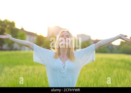 Feliz joven hermosa mujer con los brazos abiertos en el aire en un ambiente verde durante la puesta de sol. Bienestar y libertad.