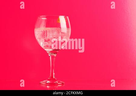 Cristal transparente de sabroso cóctel gin tonic con hielo cáscara de limón torcido en la mesa de fondo rosa Foto de stock