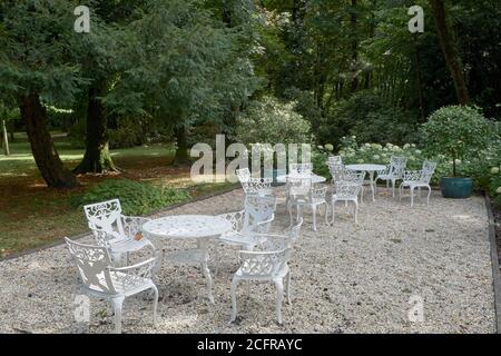 Mesas de metal pintado de blanco y sillas de grava en una terraza en un jardín en el Château de Breuil en Normandía, Francia Foto de stock