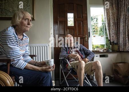 Una pareja de ancianos se sentó en su porche distanciando social en casa durante el bloqueo de la pandemia de coronavirus, Gales, Reino Unido Foto de stock