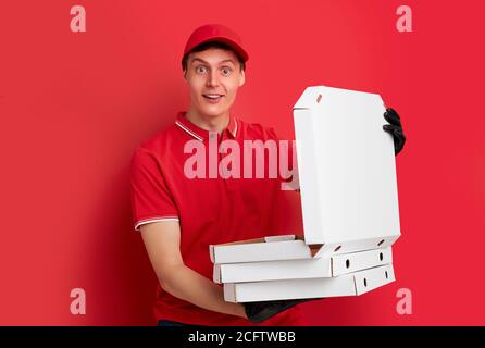 guapo hombre caucásico de entrega sosteniendo pizza en caja aislada sobre fondo rojo del estudio, entrega durante el concepto de coronavirus cuarentena.