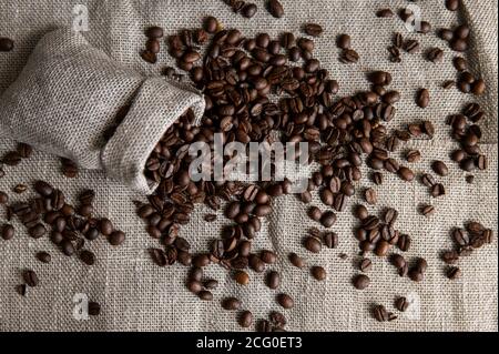 Café disperso de una bolsa de lino y una taza de café negro Espresso o  Americano de pie sobre una mesa de madera. Granos de café arábica frescos  en la ropa de