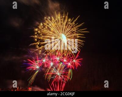 Gran flash dorado de fuegos artificiales y muchos pequeños flashes en rojo con chispas lila contra un cielo oscuro