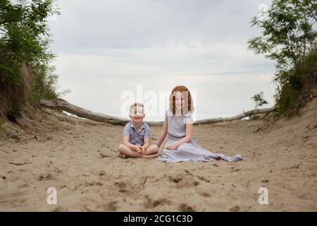 Hermanos de niño y niña sentados en una playa Presque Isle Al atardecer