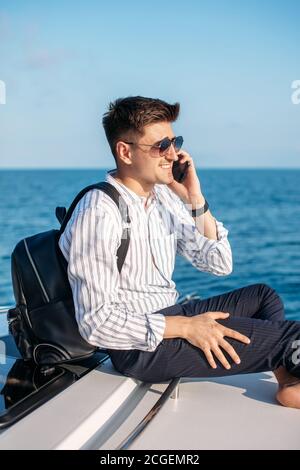 Espacio para texto. Hombre joven guapo en la ropa de oficina relajante y  hablando en el smartphone en la proa de la lancha motora, sobre el fondo  del mar Fotografía de stock -