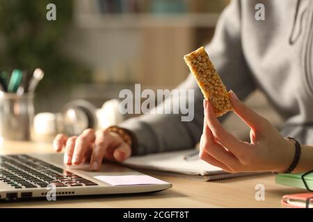 Primer plano de las manos de la estudiante sosteniendo el snack bar earning nocturno en el ordenador portátil