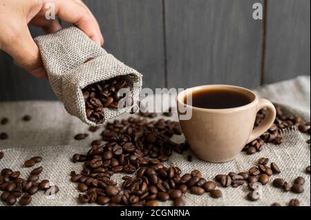 Café disperso de una bolsa de lino y una taza de café negro Espresso o  Americano de pie sobre una mesa de madera. Granos de café arábica frescos  en la ropa de cama Fotografía de stock - Alamy