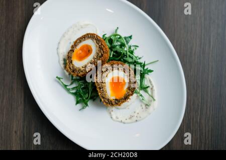 Huevo escocés cortado a la mitad con yema de oro servido Una ensalada de placas y cohetes
