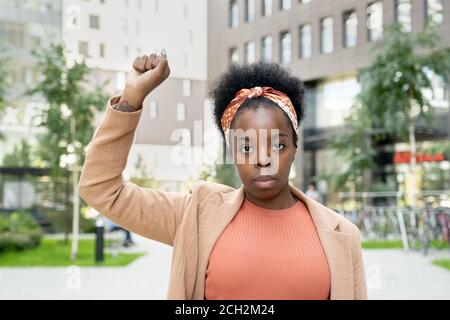 Joven empresaria contemporánea de etnia africana manteniendo el brazo derecho levantado