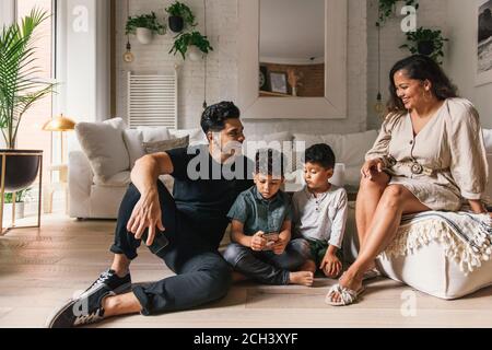 Mamá y papá riendo mientras los niños pequeños juegan teléfono en la sala de estar