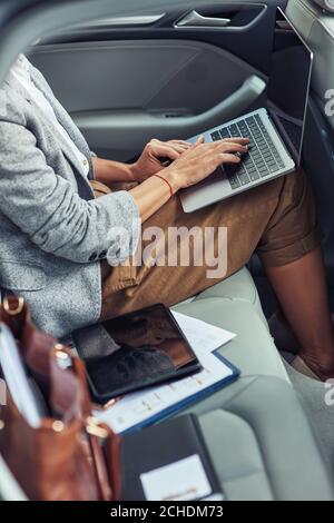 Trabajando en línea en taxi, disparo vertical de la mujer de negocios utilizando el portátil mientras se sienta en el asiento trasero en el coche