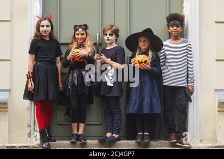 Retrato completo de un grupo multiétnico de niños que visten Halloween disfraces mirando la cámara mientras trampean o tratan juntos