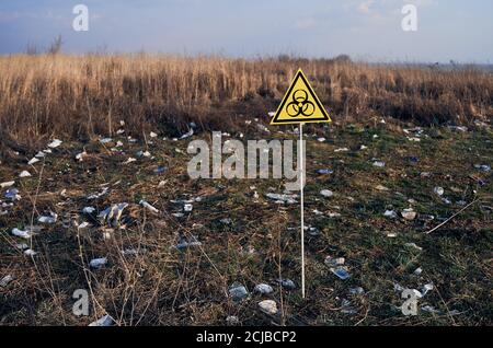 Triángulo amarillo con símbolo de peligro biológico advertencia en territorio abandonado con basura. Campo de basura con señal de peligro biológico. Concepto de ecología, contaminación ambiental y peligro.