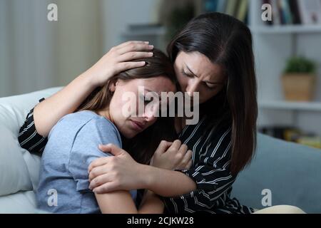 Triste adolescente llorando siendo consolada por su hermana en un sofá en la sala de estar en casa