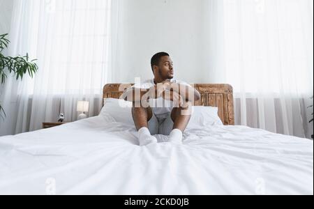 Hombre afroamericano pensativo mirando a un lado sentado en el dormitorio interior Foto de stock