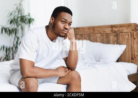 Infeliz Black Guy sentado en la cama en el dormitorio en casa Foto de stock