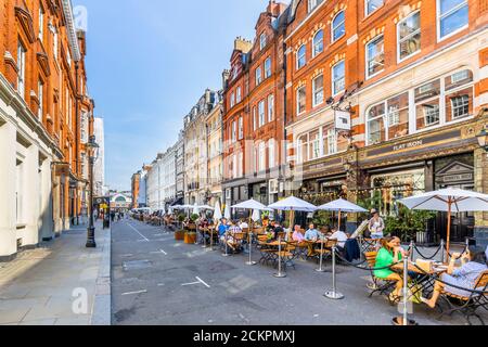 Al aire libre al borde de la carretera almuerzo socializar, cenar, comer y beber en la calle peatonal Henrietta, Covent Garden, Londres WC2 en un día soleado Foto de stock