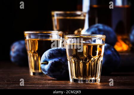Slivovica - brandy de ciruela o vodka de ciruela, licor fuerte, bebida fuerte en vasos en la vieja mesa de madera, ciruelas frescas, espacio de copia Foto de stock