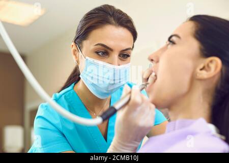 Un dentista serio que elimina el cálculo de los dientes del cliente con un escalador ultrasónico en la clínica dental moderna Foto de stock