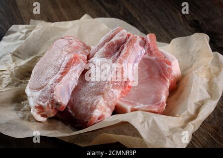 Un montón de filetes de cerdo cruda picada fresca a lo largo de los huesos en el papel de envolver en la mesa. Close-up. Foto de stock