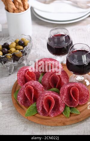 Comida ligera bocadillo de salami doblado en forma de flor con un vaso de vino de Jerez en un plato de madera. Foto de stock