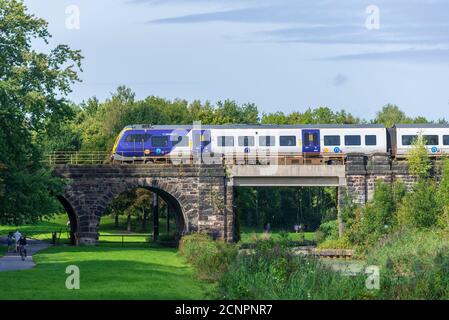 Un tren diesel Northern Rail cruza el viaducto de Sankey Valley sobre el canal en desuso en el parque linaer en el oeste de Warrington. Foto de stock