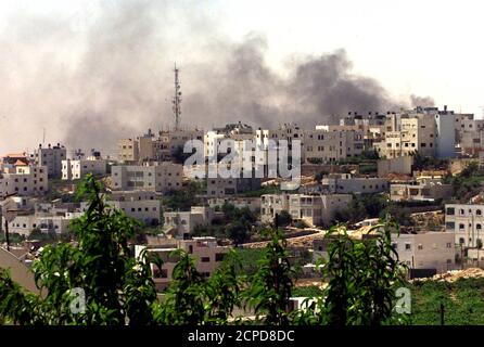 El humo se eleva sobre la ciudad de Hebrón, en la Ribera Occidental, el 26 de junio de 2002, durante el bombardeo del edificio de la policía palestina por las fuerzas israelíes. Israel mantuvo a los palestinos bajo el arma en siete ciudades de la Ribera Occidental y amenazó con ampliar la operación. La Autoridad Palestina, bajo la presión del Presidente de los Estados Unidos George W. Bush para deshacerse de Yasser Arafat como su líder, anunció que las elecciones presidenciales se celebrarían el próximo enero. REUTERS/Nayef Hashlamoun RS/CLH/