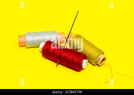 tres carretes de hilos de color y una aguja en un fondo amarillo Foto de stock