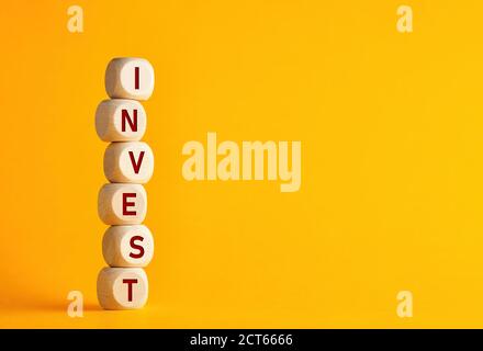La palabra invertir en cubos de madera contra fondo amarillo. Crecimiento de la inversión financiera o decisión de inversión en concepto de negocio.
