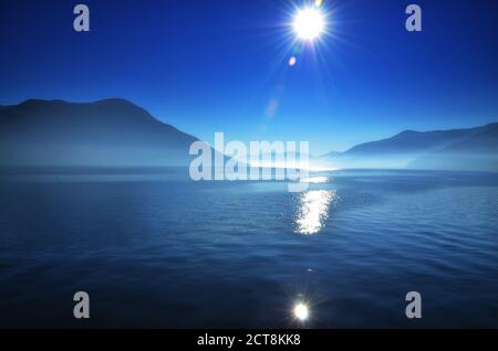 Lago alpino de niebla Maggiore con rayos de sol y montaña en Ticino, Suiza. Foto de stock