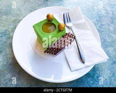 Postre de pastel cúbico de pera verde con esferas doradas arriba y parrilla  de chocolate en un lado sobre un plato blanco sobre una mesa azul  Fotografía de stock - Alamy