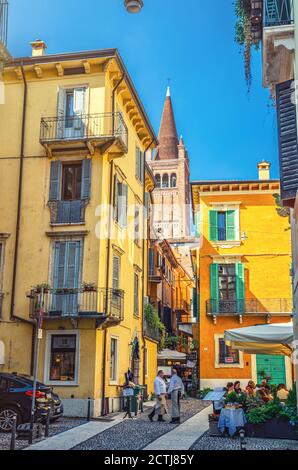 Verona, Italia, 12 de septiembre de 2019: Típica calle italiana con edificios tradicionales con ventanas de obturación, restaurante de calle, foto de estilo retro, torre de la Basílica de Santa Anastasia iglesia